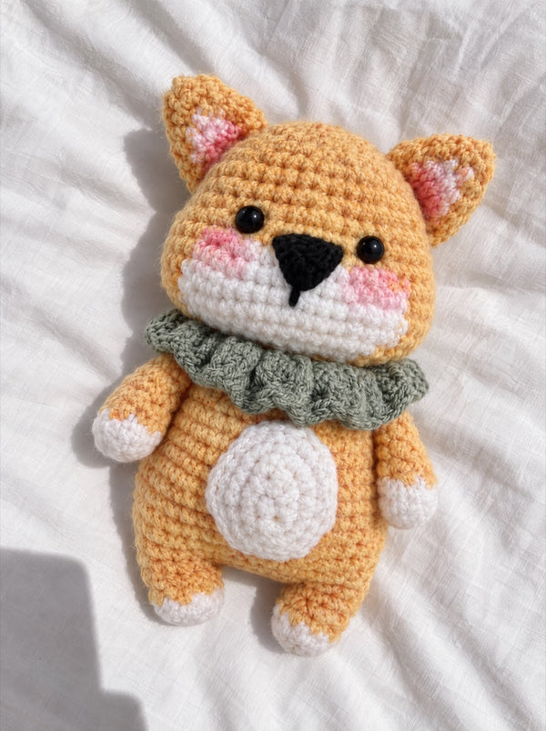 Crocheted shiba with a green collar on a white sheet