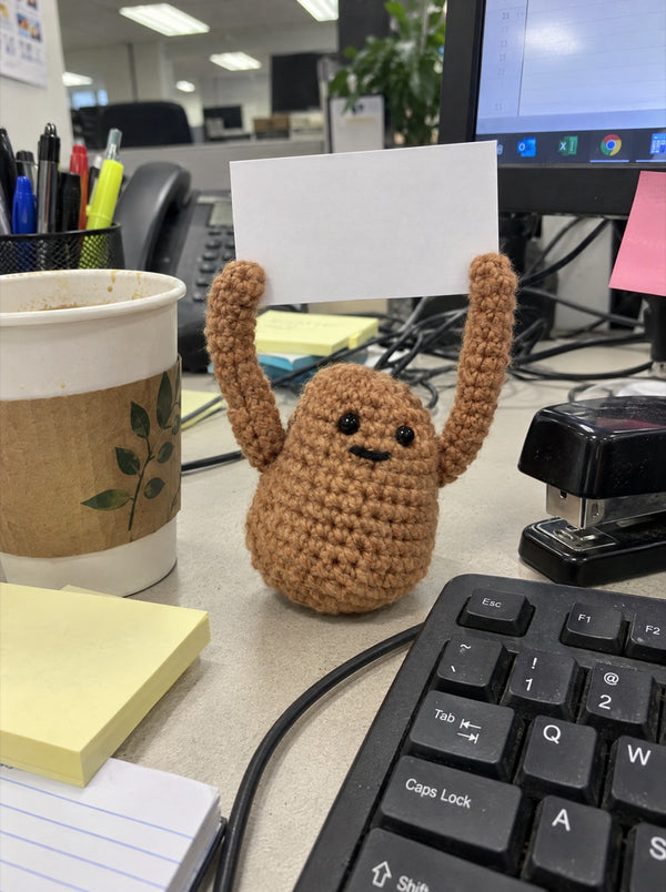 Crocheted potato holding a sign on an office desk next to a keyboard