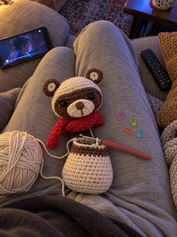 Crocheted bear with a red scarf in progress, with yarn and hook on a sofa