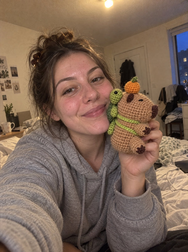 Smiling young woman holding a crocheted capybara with a turtle and an orange